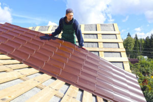 Worker Puts The Metal Tiles On The Roof Of A Wooden House